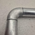 Uni‑Fit 90 degree elbow joiner connecting two steel barrier pipes on textured surface