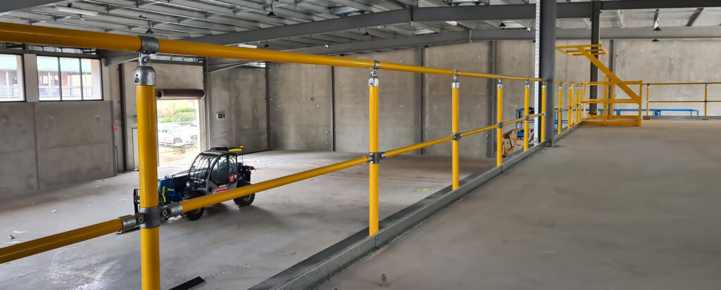 A yellow Uni-fit safety handrails with galvanised pipe fittings installed along the edge of an industrial mezzanine