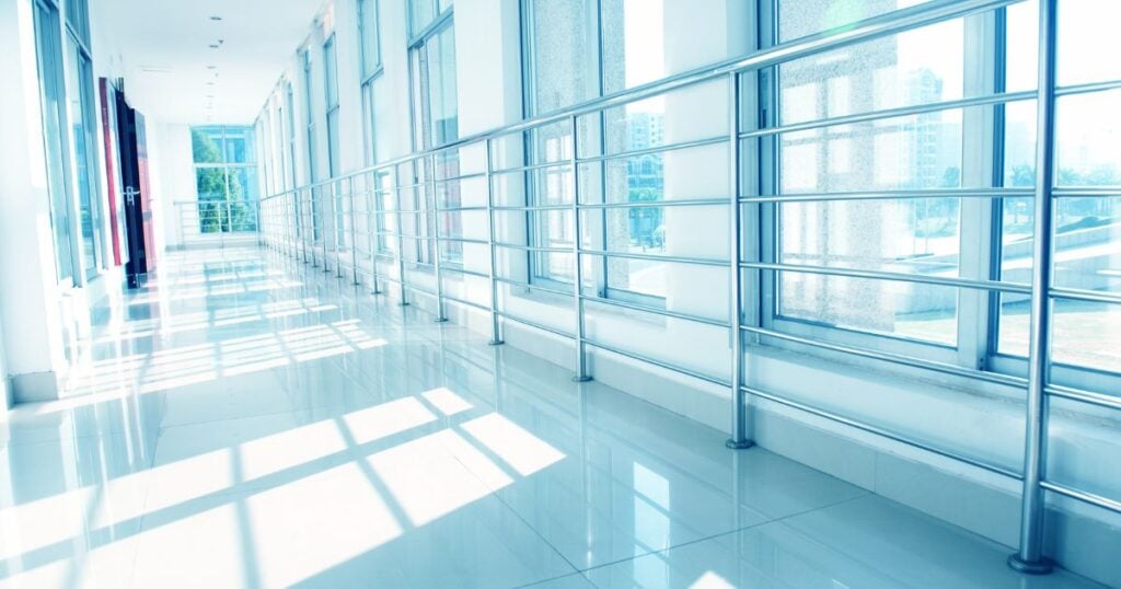 Stainless steel dual handrail system along a tiled corridor with floor-to-ceiling windows in a hospital