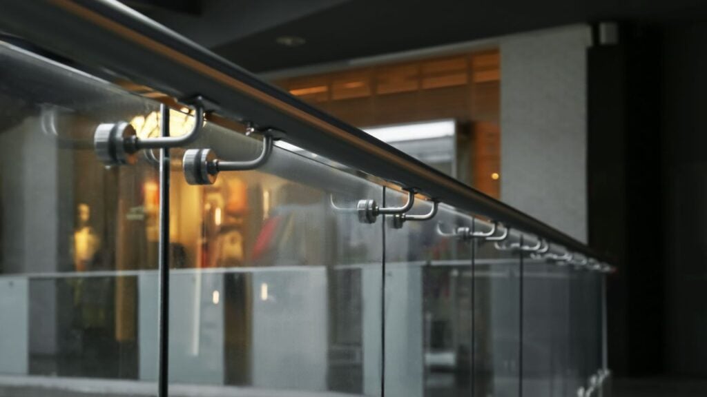 Black steel handrail mounted on glass panels with metal clamp fixings inside a shopping centre